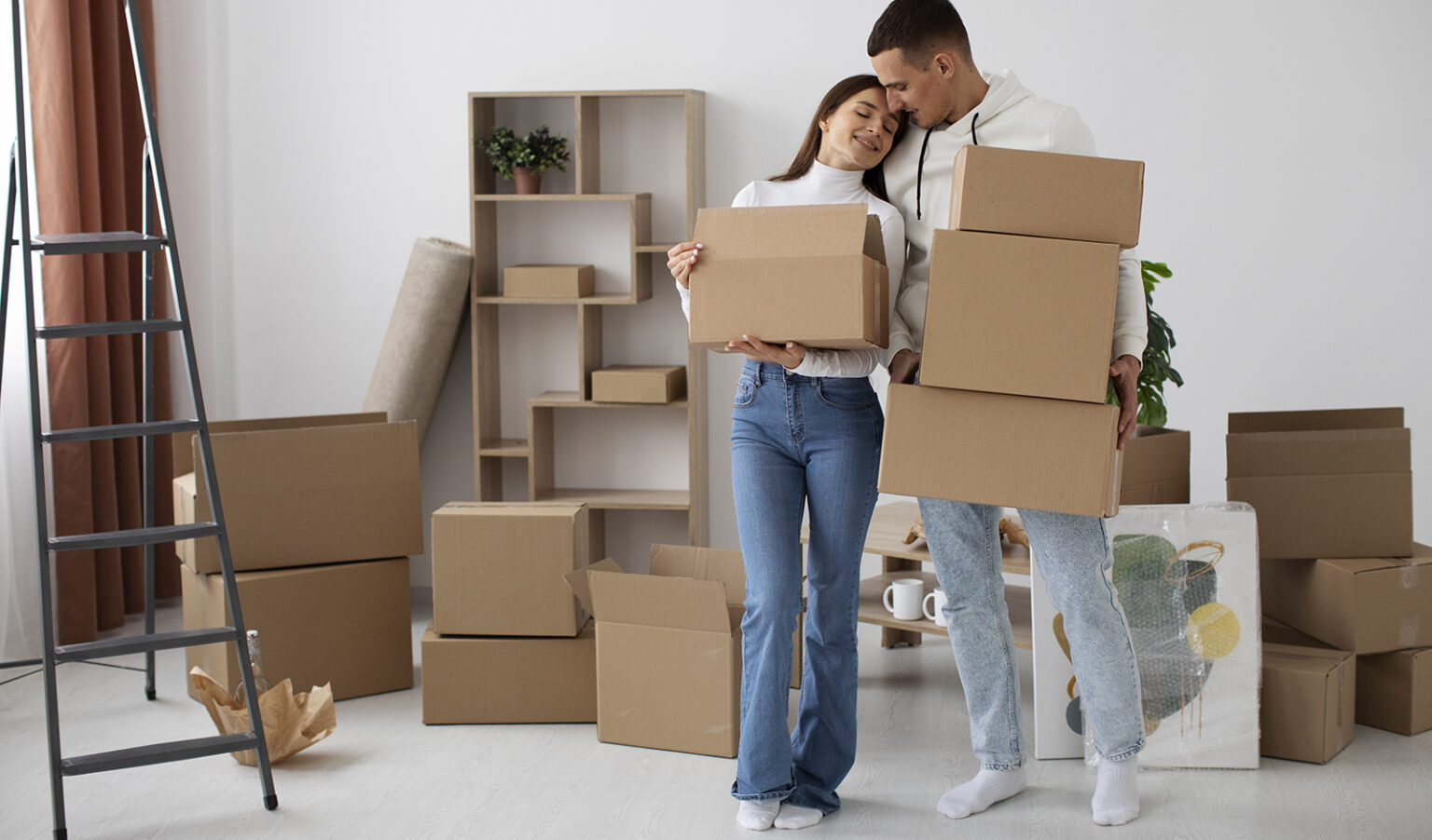 A couple holding moving boxes, smiling in their new home